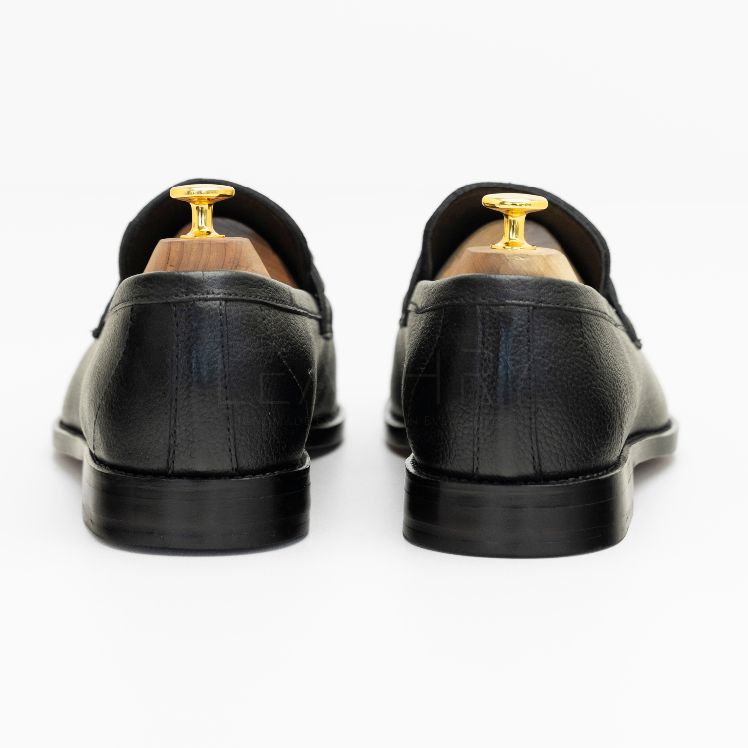 Black leather loafers with gold tips on a white background