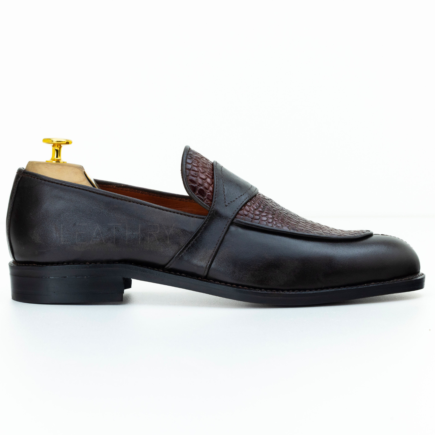 Black leather loafer with brown textured strap on a white background