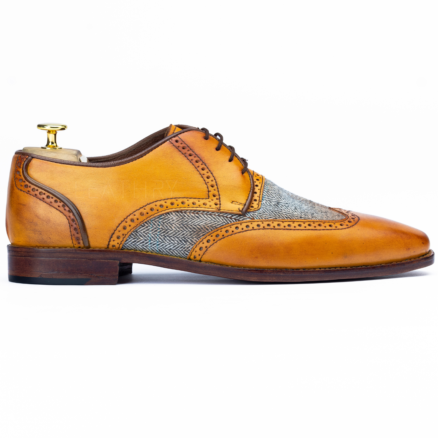 Brown leather dress shoe with patterned patch on a white background