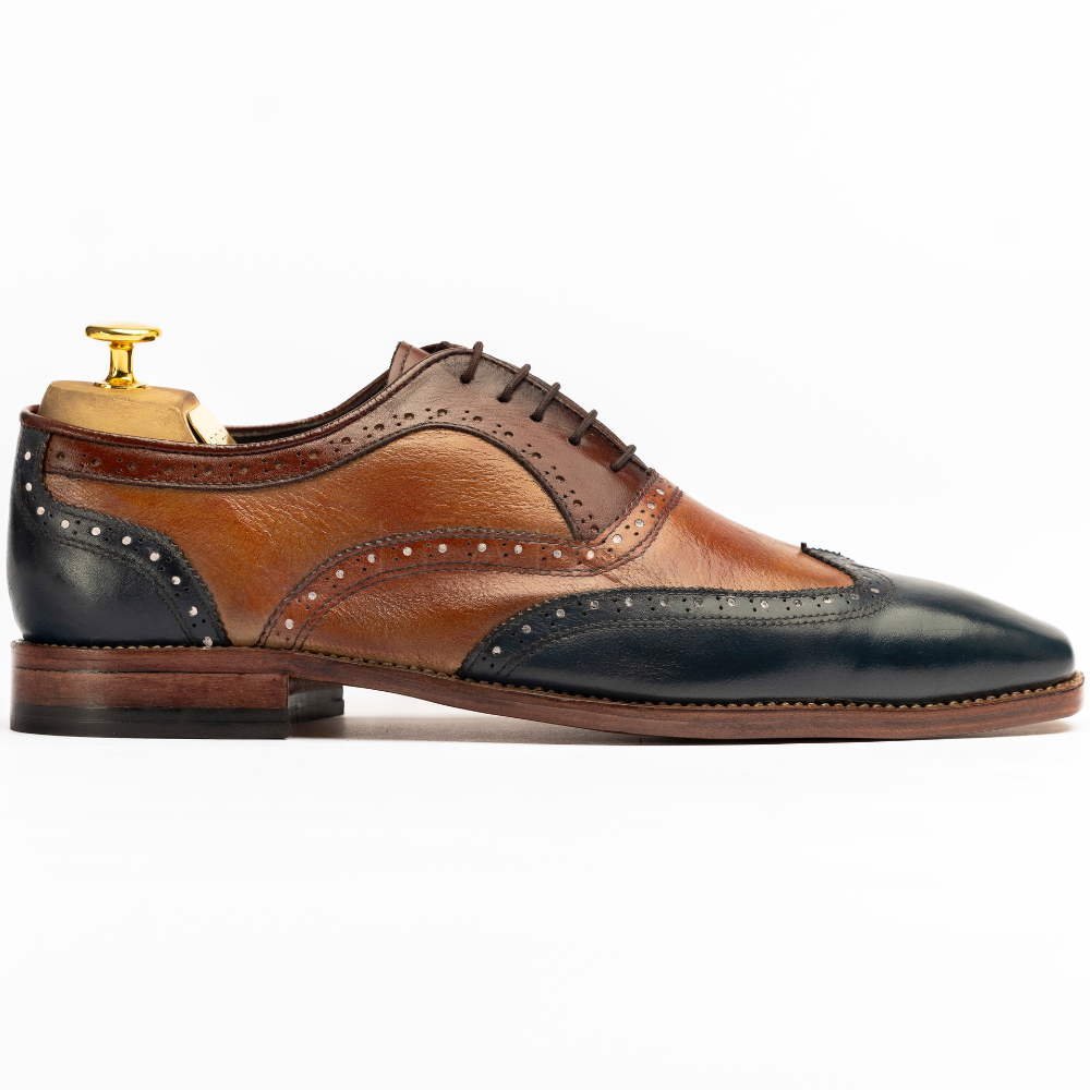 Brown and black leather dress shoe with wingtip design on a white background