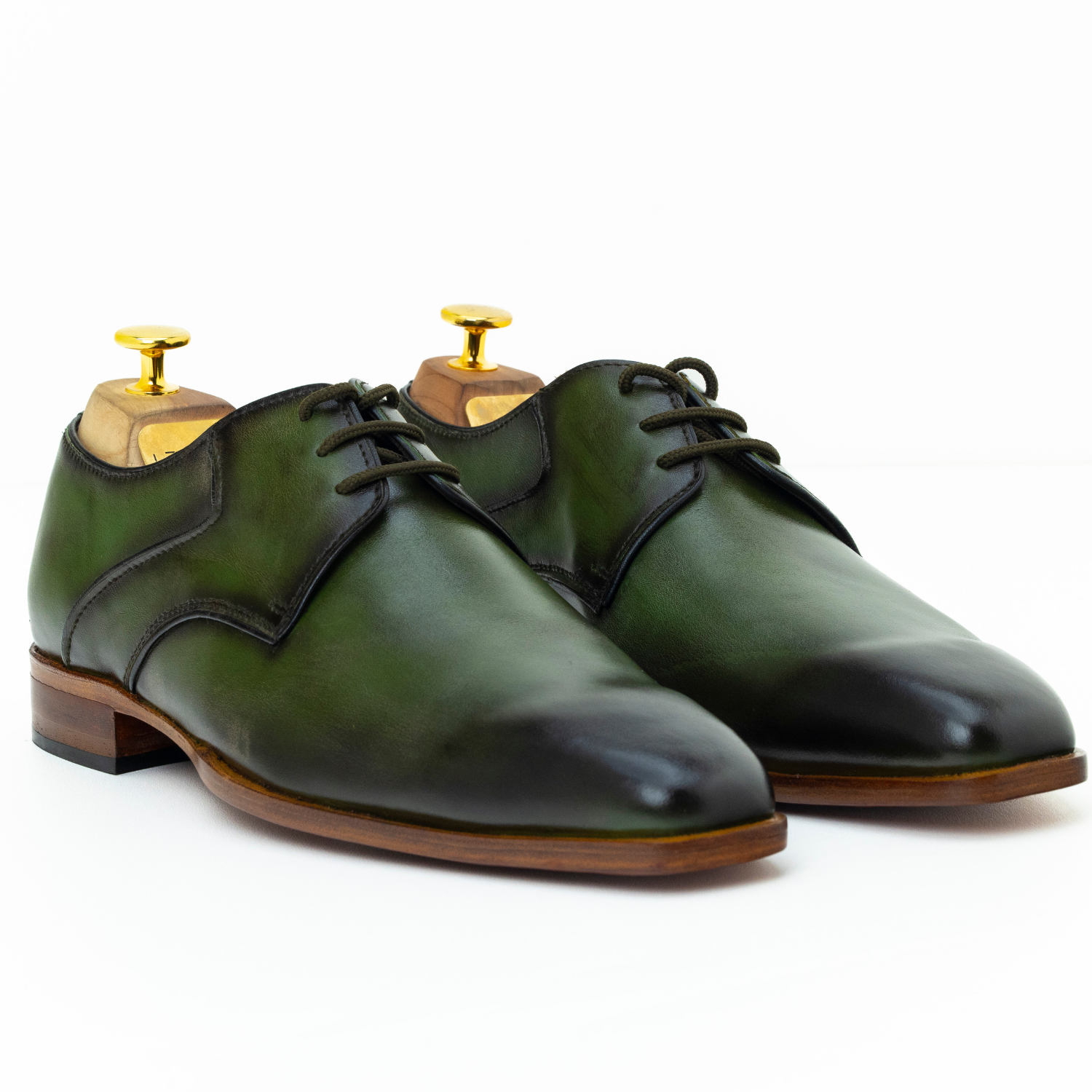 Green leather shoes with black accents on wooden dress forms against a white background