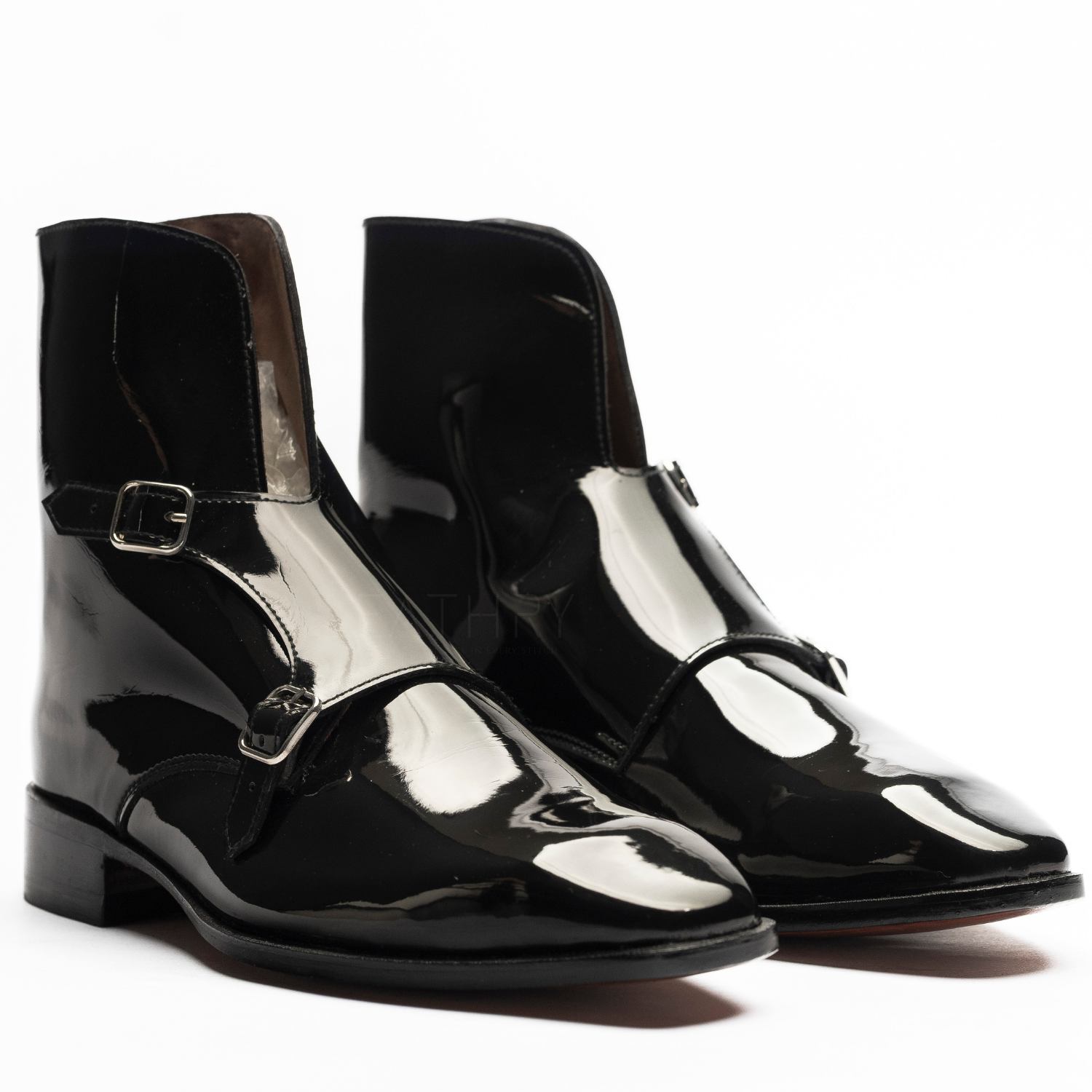 Pair of black patent leather boots with buckles on a white background