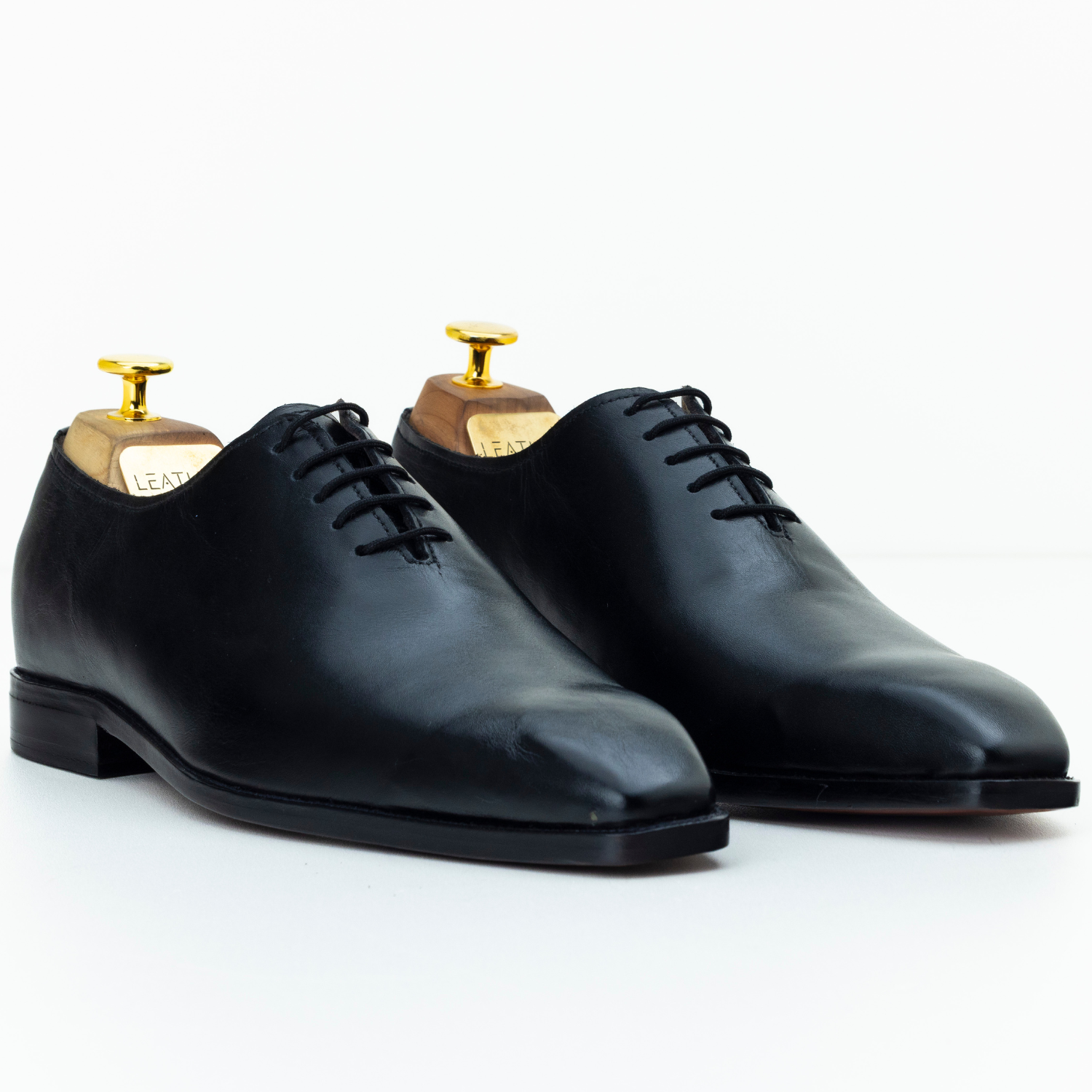 Pair of black dress shoes with gold dressers on a white background