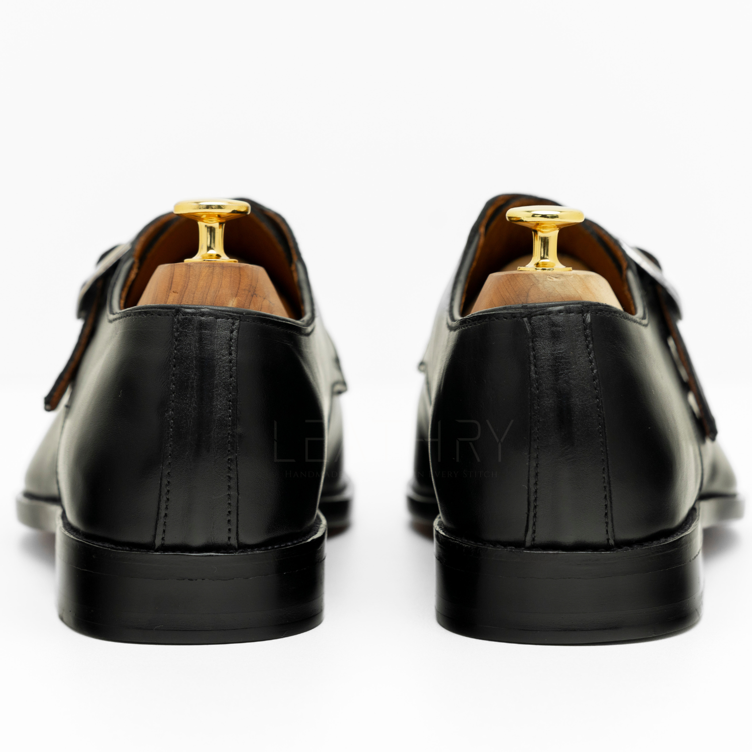 Black leather shoes with gold accents on a white background