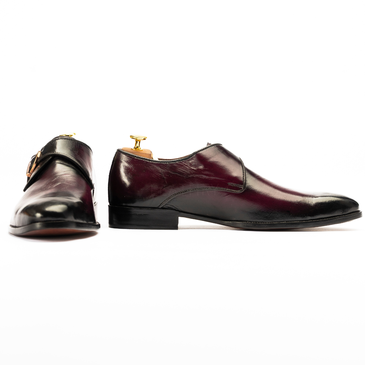 Pair of polished leather shoes with gold buckles on a white background