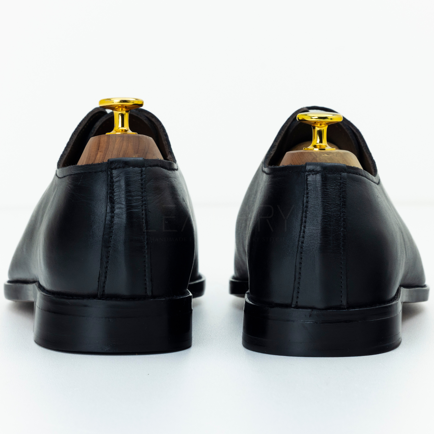 Black leather shoes with gold accents on a white background