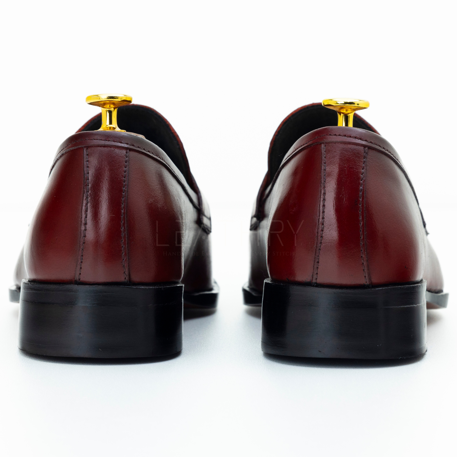 Pair of maroon leather shoes with gold accents on a white background