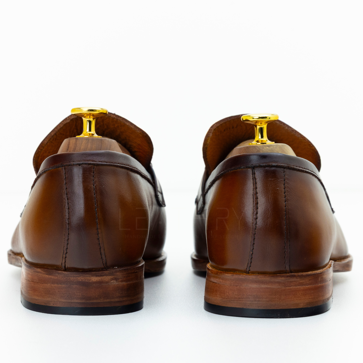 Brown leather loafers with gold accents on a white background
