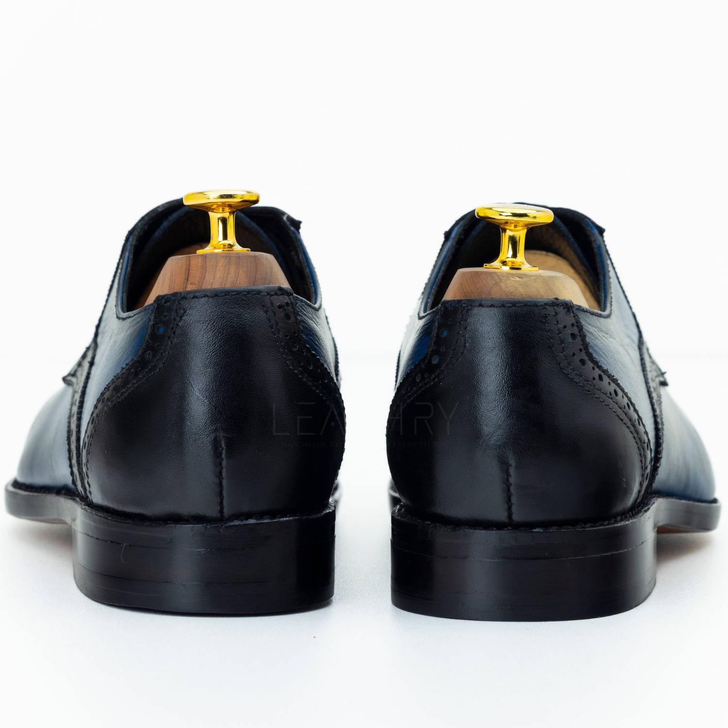 Black leather dress shoes with gold accents on a white background