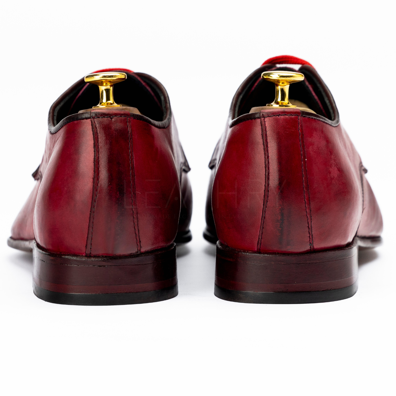 Pair of red leather shoes with gold dress studs on a white background
