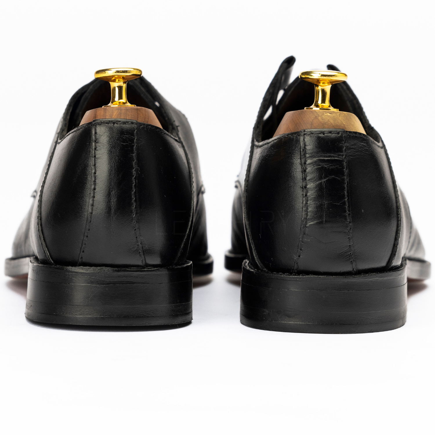 Black leather shoes with gold accents on a white background