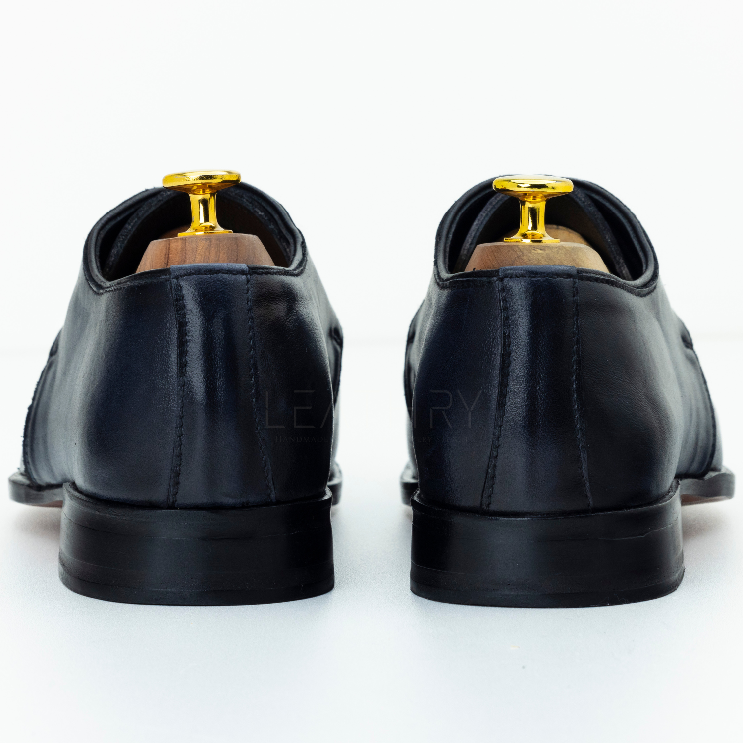 Black leather shoes with gold accents on a white background