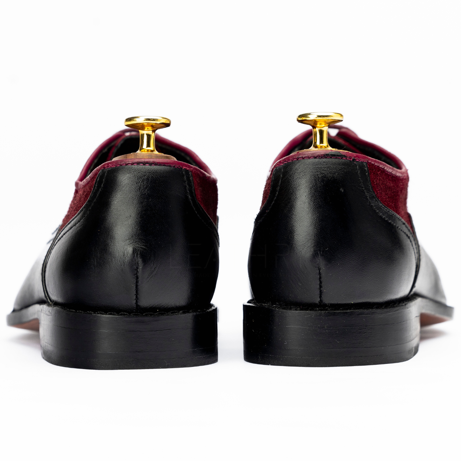 Pair of maroon and black dress shoes with gold dress studs on a white background
