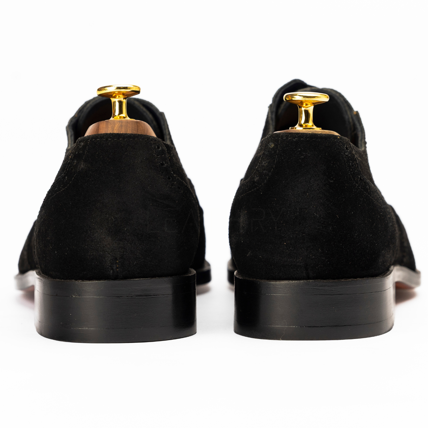 Black suede shoes with gold tips on a white background