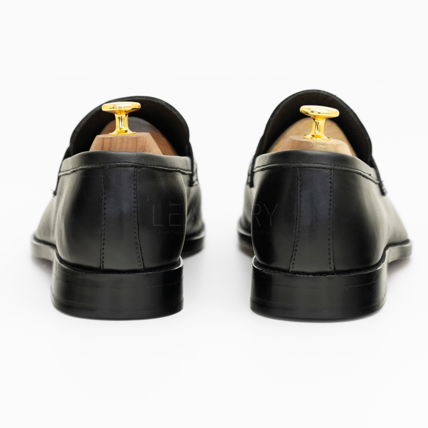 Black leather loafers with gold tips on a white background