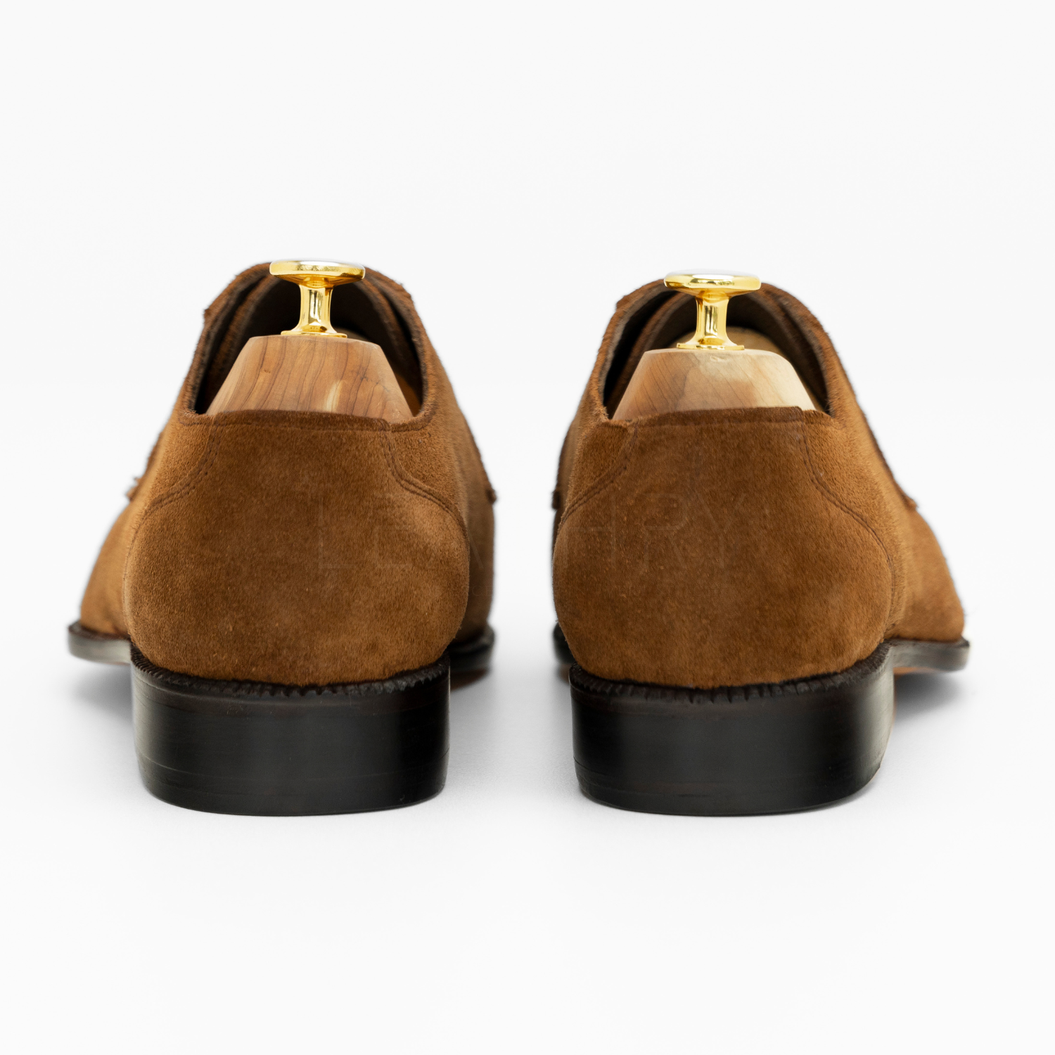 Brown suede shoes with gold accents on a white background