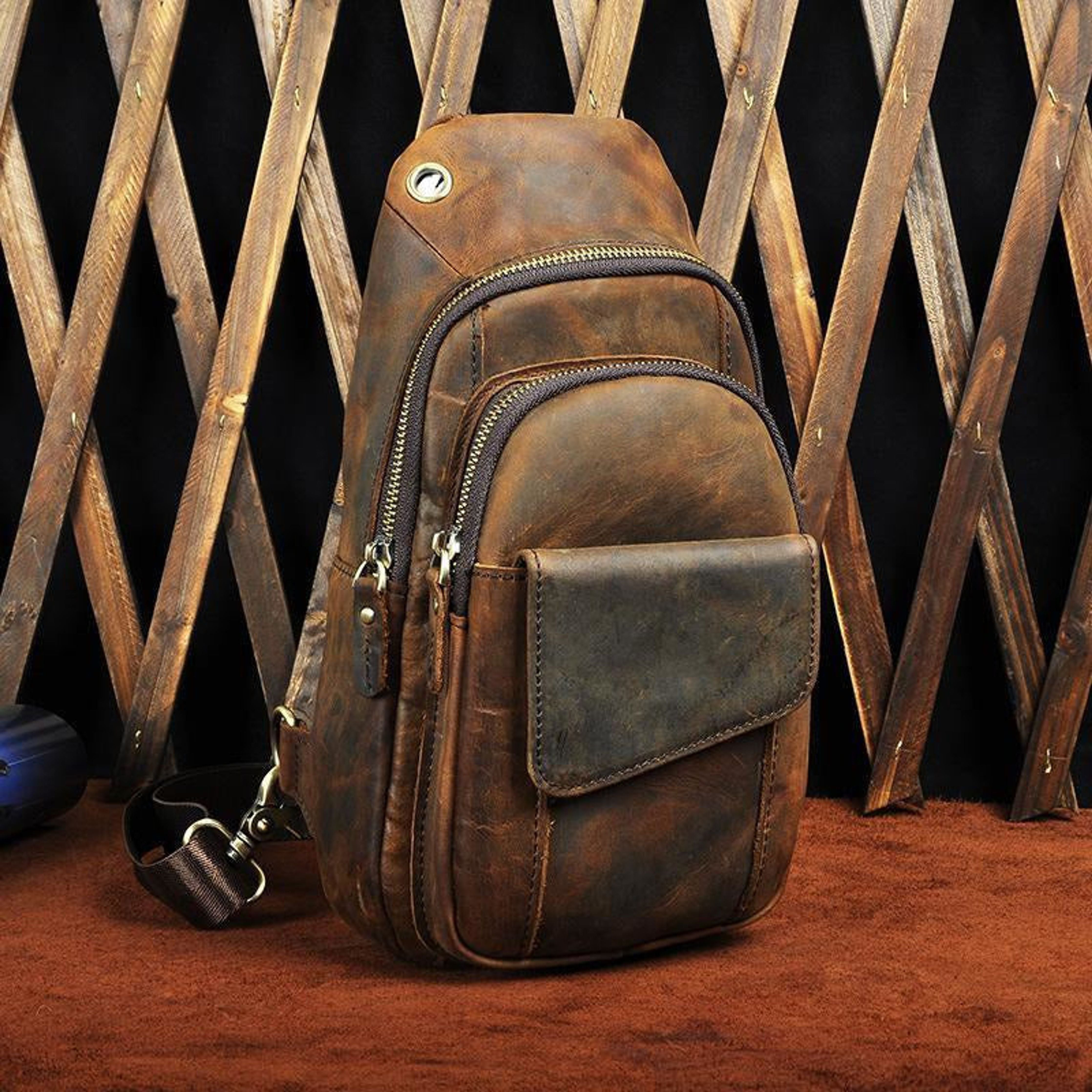 Brown leather sling bag with multiple zippers against a wooden lattice background