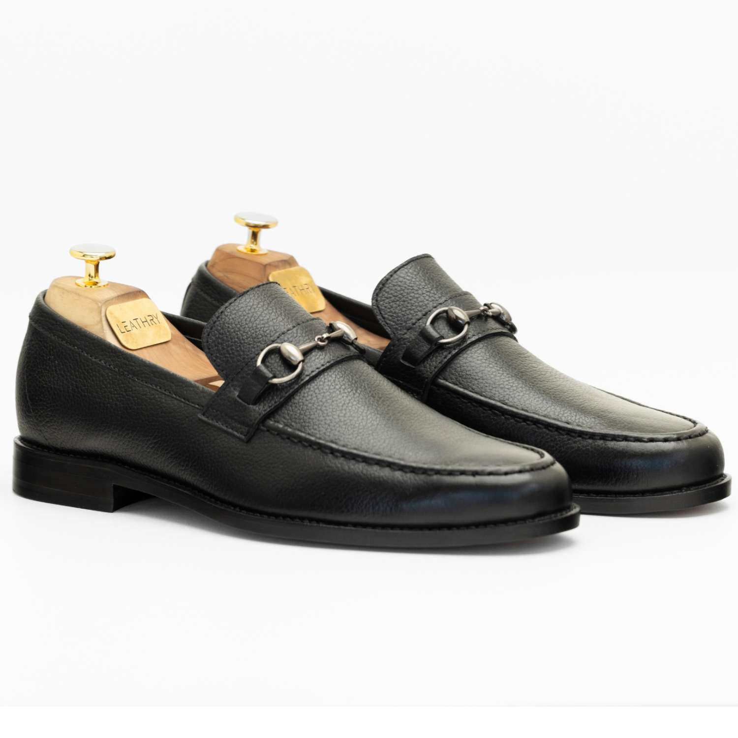 Pair of black leather loafers with gold hardware on a white background