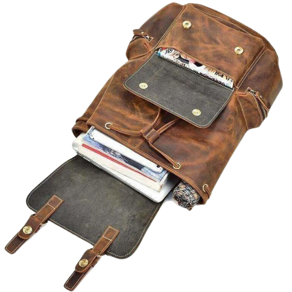 Brown leather backpack with open front pocket showing books and a magazine on a white background