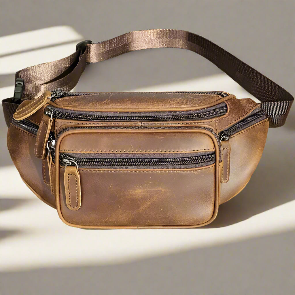 Brown leather waist bag with multiple zippers on a light background