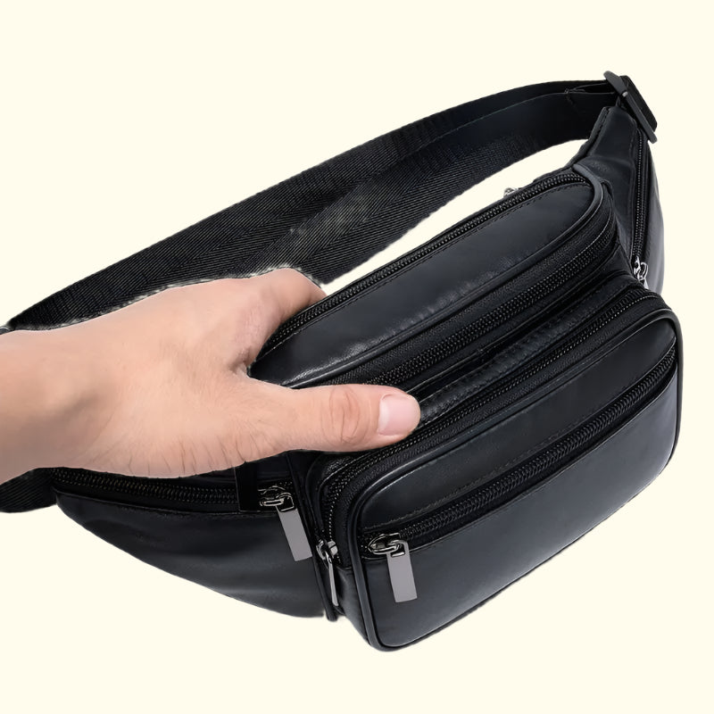 Black waist bag with multiple zippers held by a hand on a white background