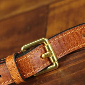 Close-up of a brown leather belt with a brass buckle on a wooden surface