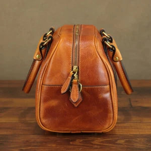 Brown leather bag with gold zippers on a wooden surface