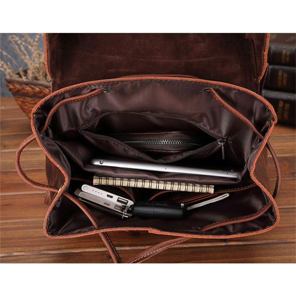 Brown leather bag with compartments containing stationery items on a wooden surface.