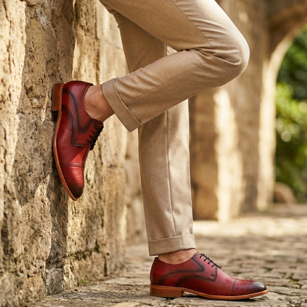 Red leather shoes worn with beige pants against a stone wall and cobblestone path background.