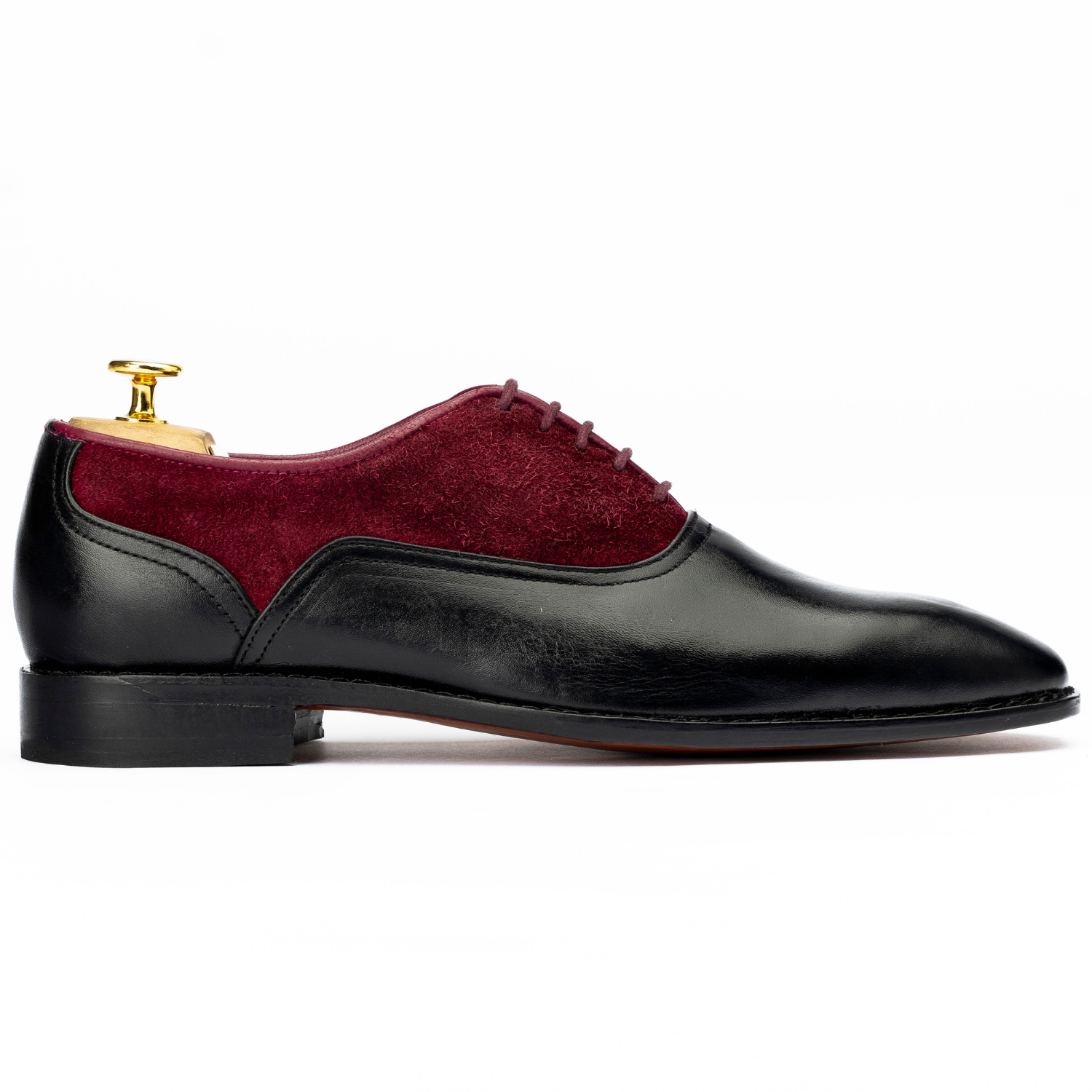 Black dress shoe with red suede side panel on a white background