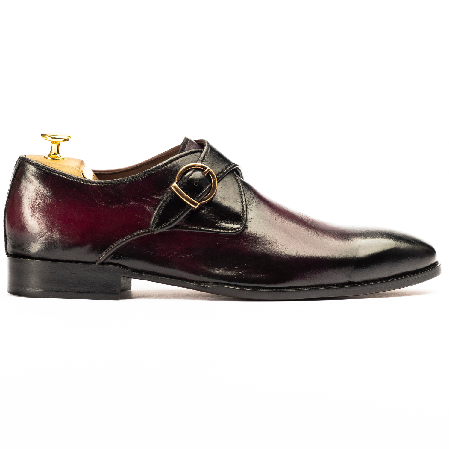 Shiny black dress shoe with a gold buckle on a white background