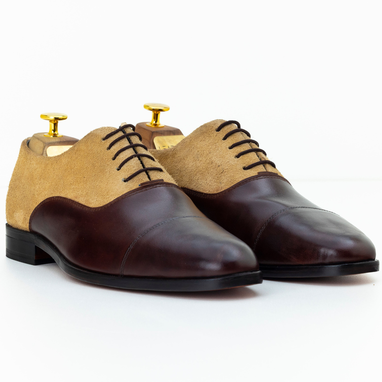 Pair of brown and beige dress shoes with gold dress studs on a white background
