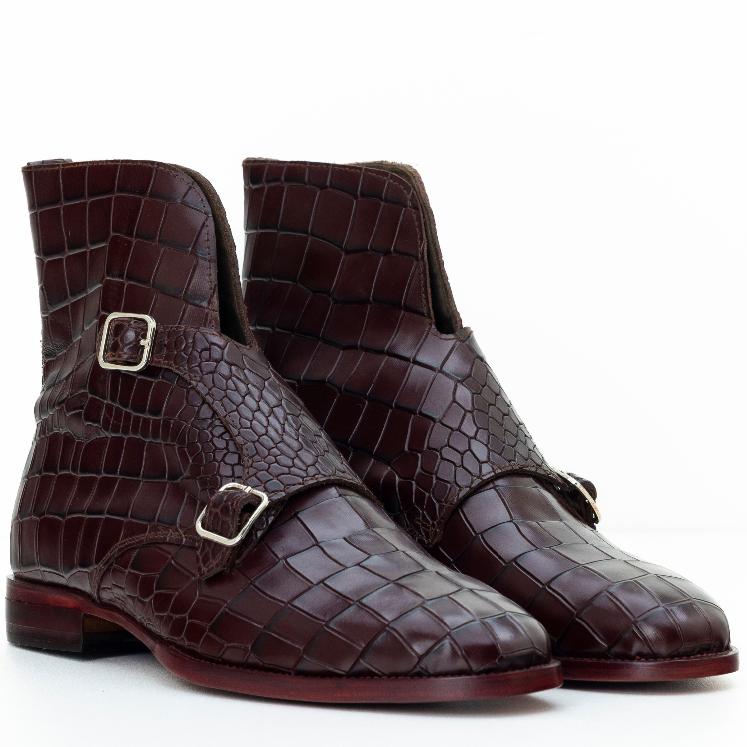Pair of brown crocodile-patterned boots with gold buckles on a white background