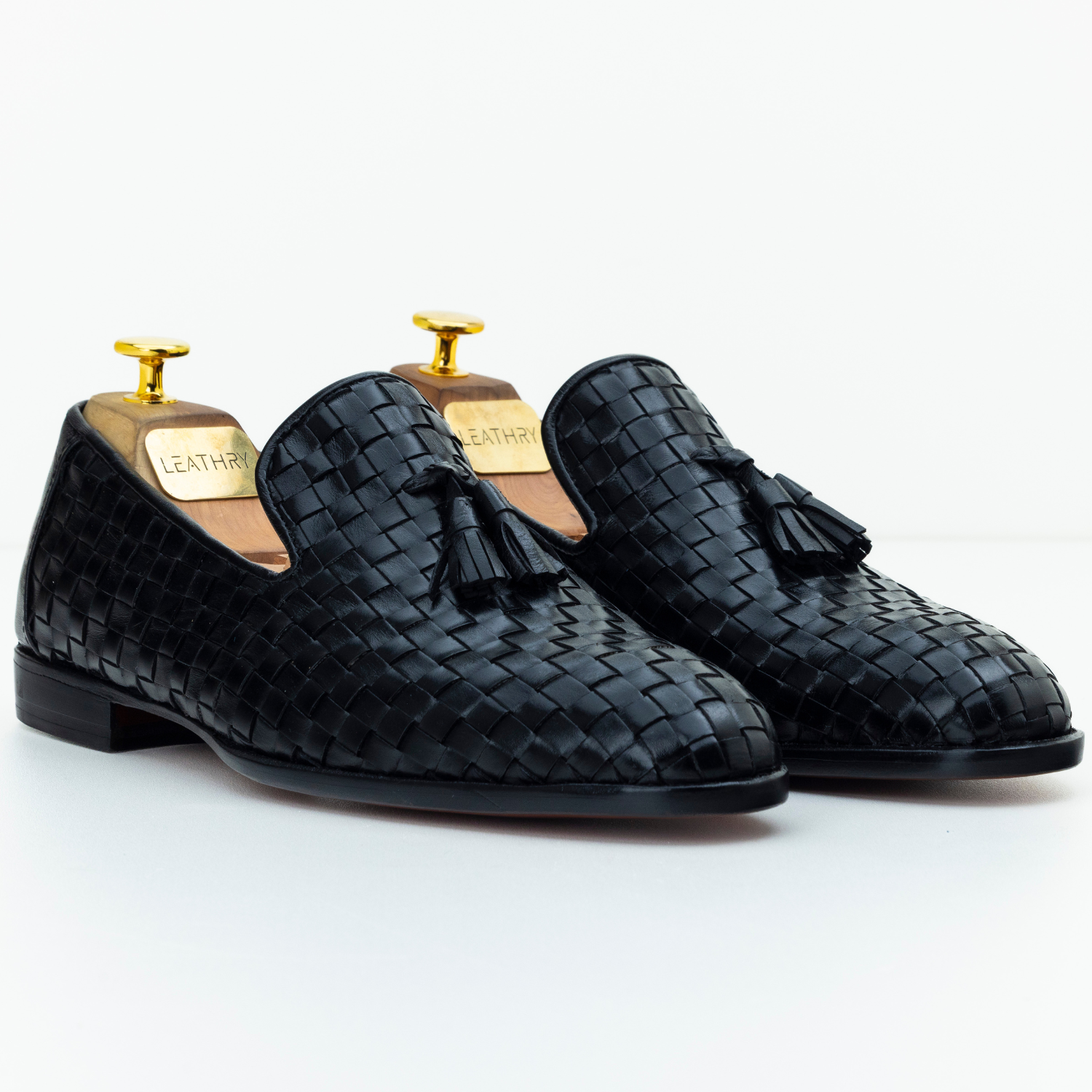Pair of black woven loafers with tassels on a white background