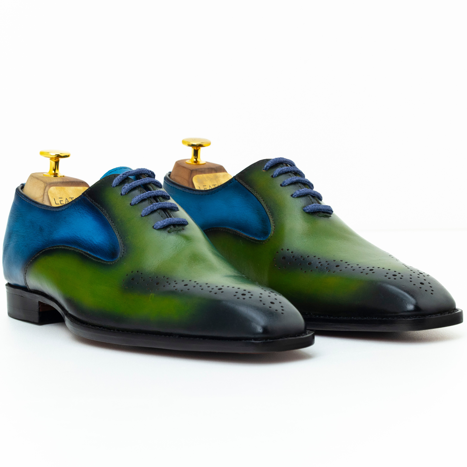 Green and blue dress shoes with gold dress studs on a white background