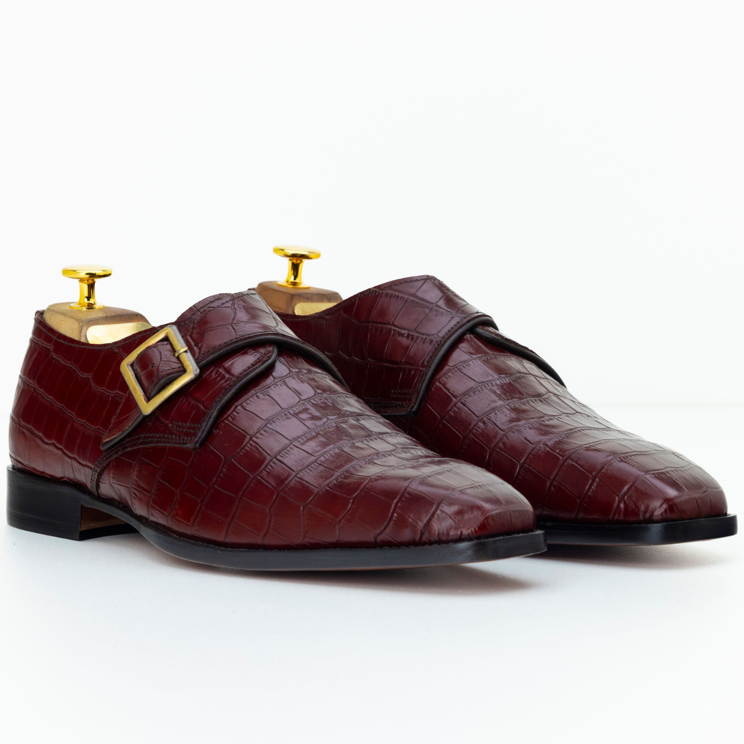 Pair of maroon leather shoes with gold buckles on a white background