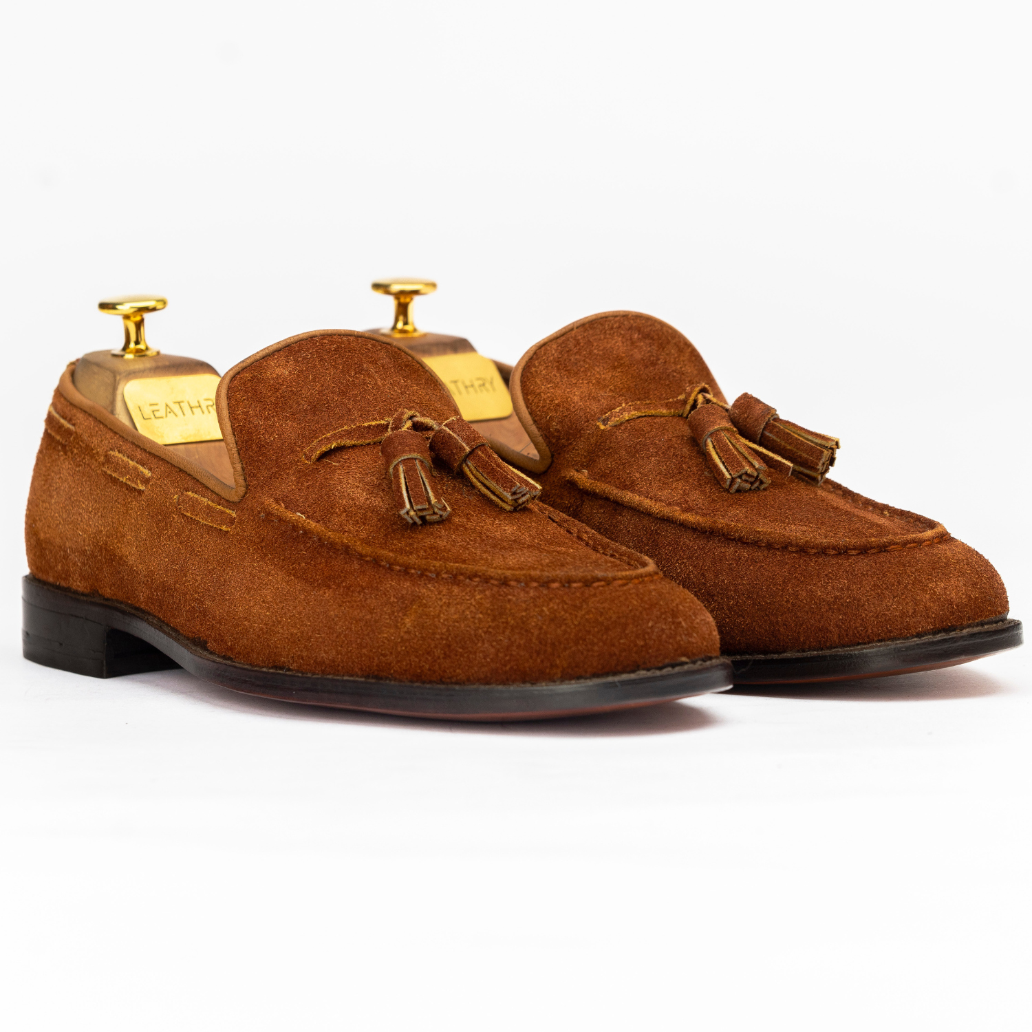 Pair of brown suede loafers with tassels on a white background
