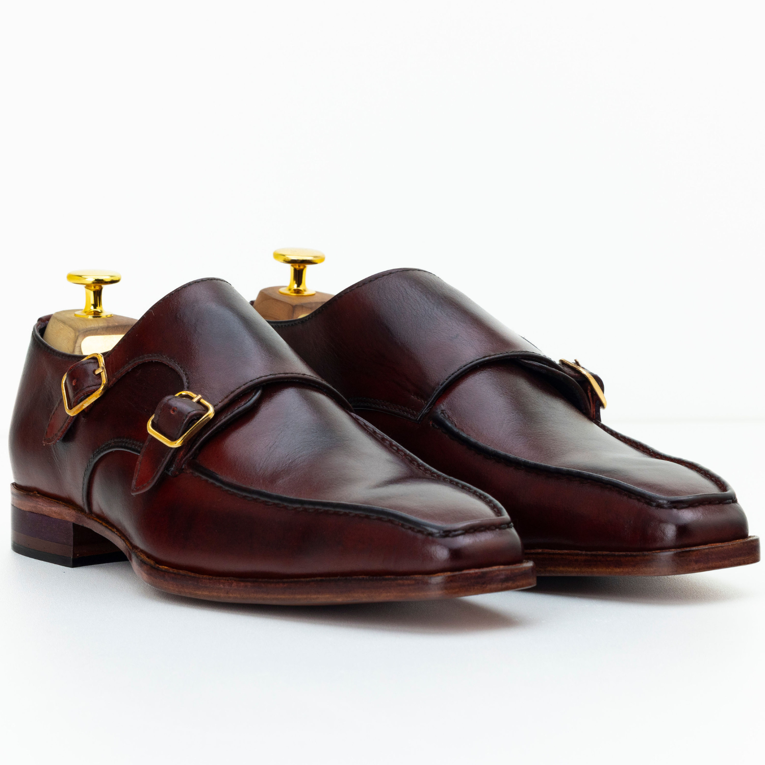 Pair of brown leather monk shoes with gold buckles on a white background