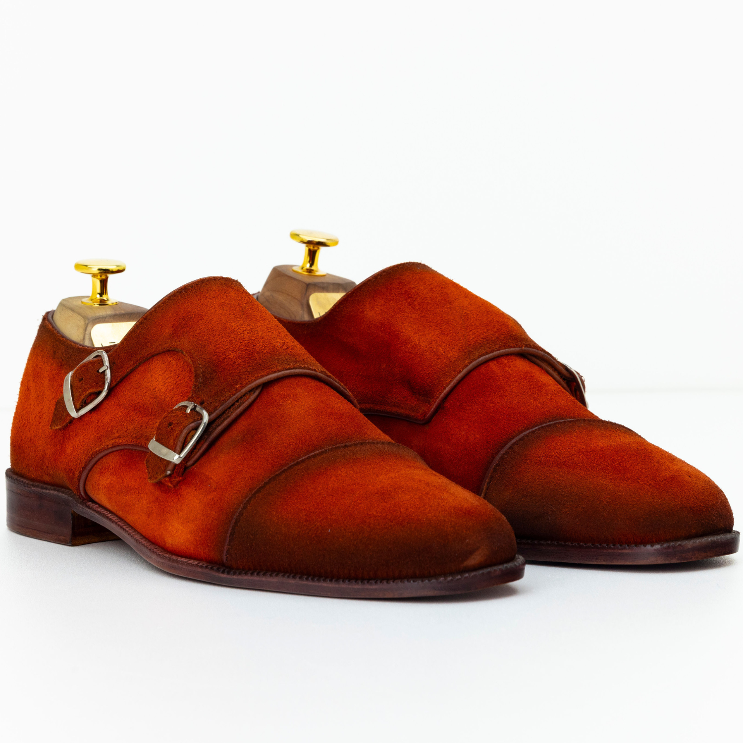 Pair of brown suede shoes with gold buckles on a white background