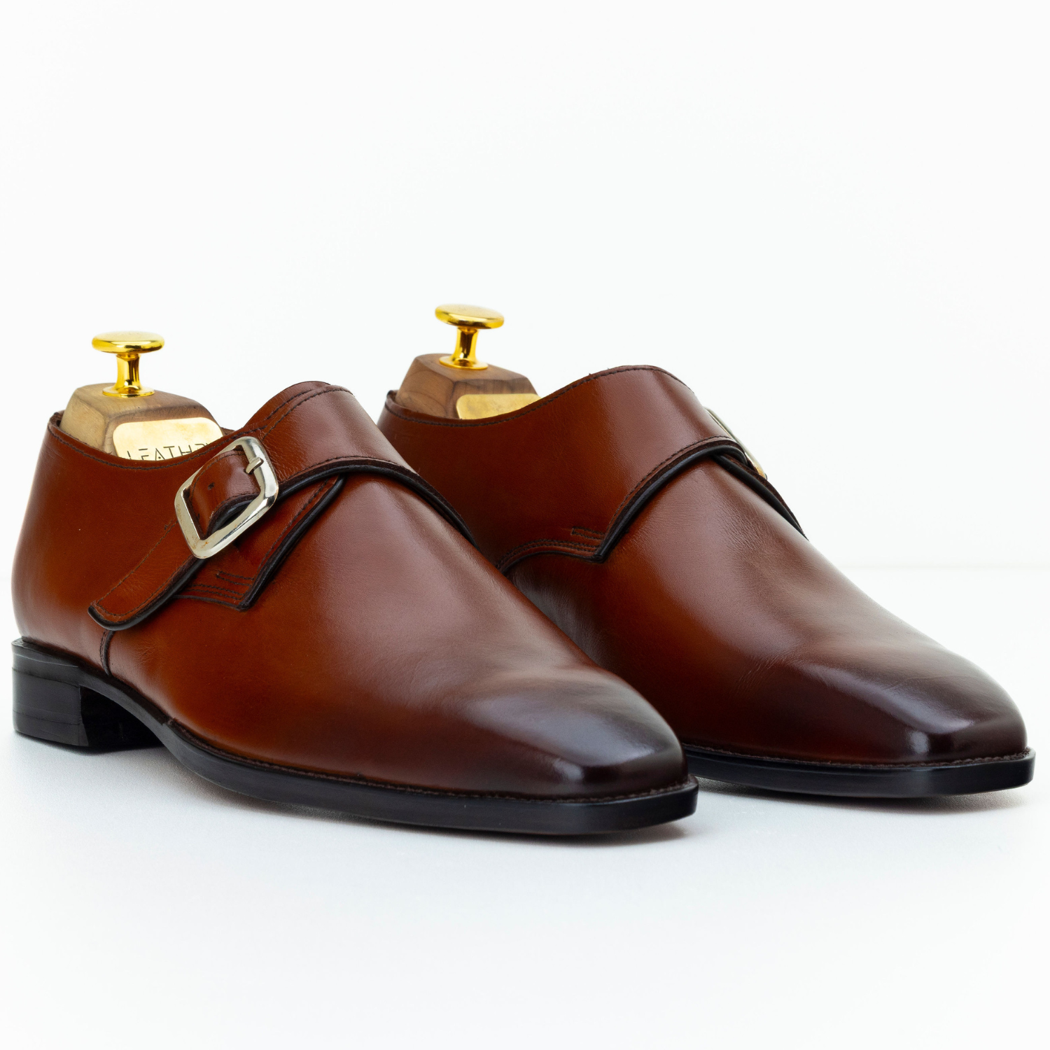 Pair of brown leather shoes with gold buckles on a white background