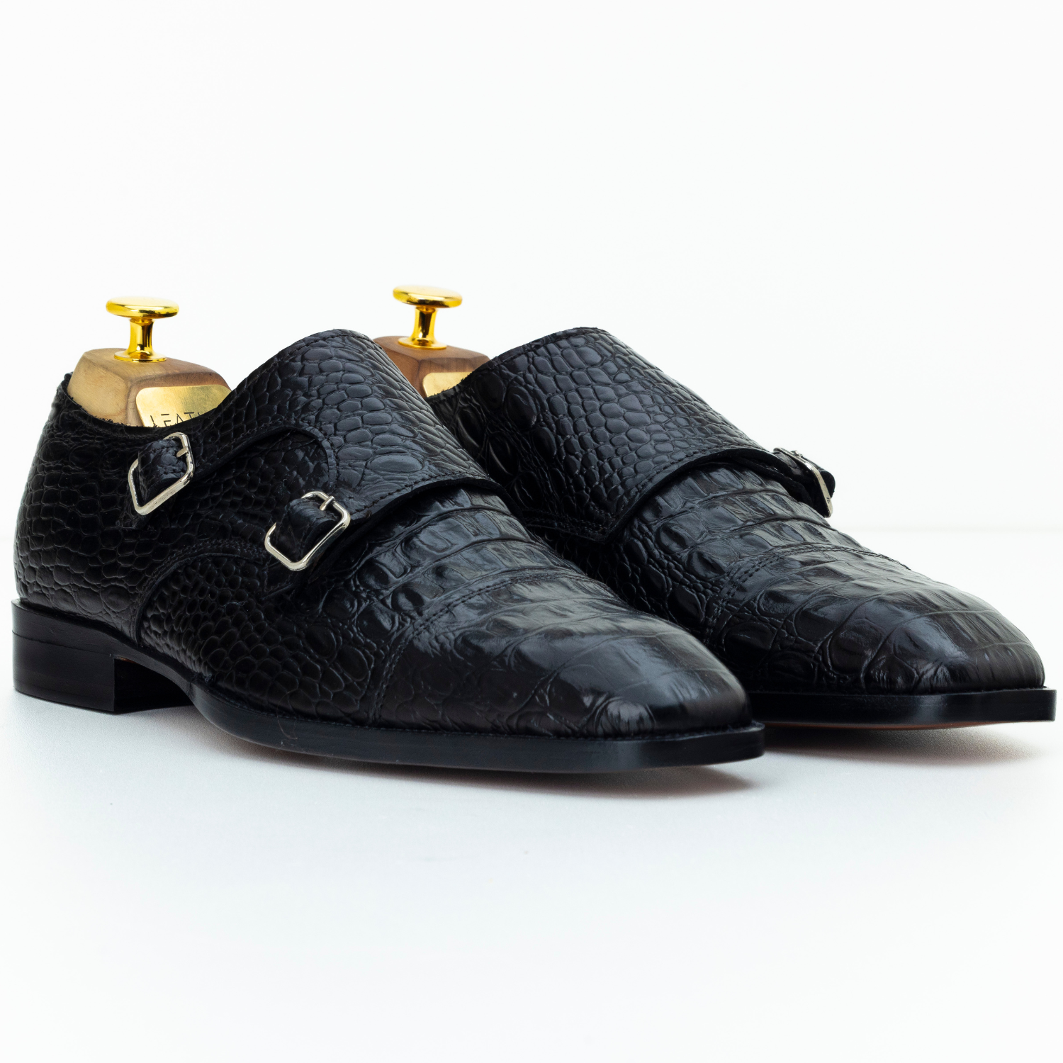 Pair of black textured dress shoes with gold buckles on a white background
