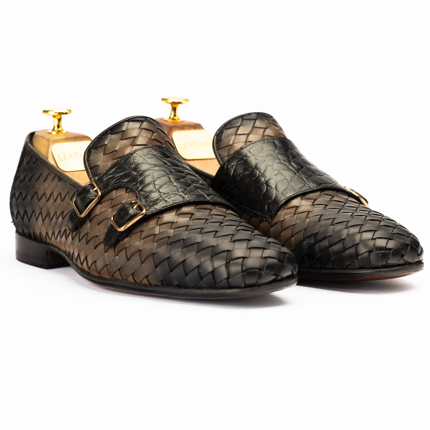 Pair of woven black shoes with gold buckles on a white background