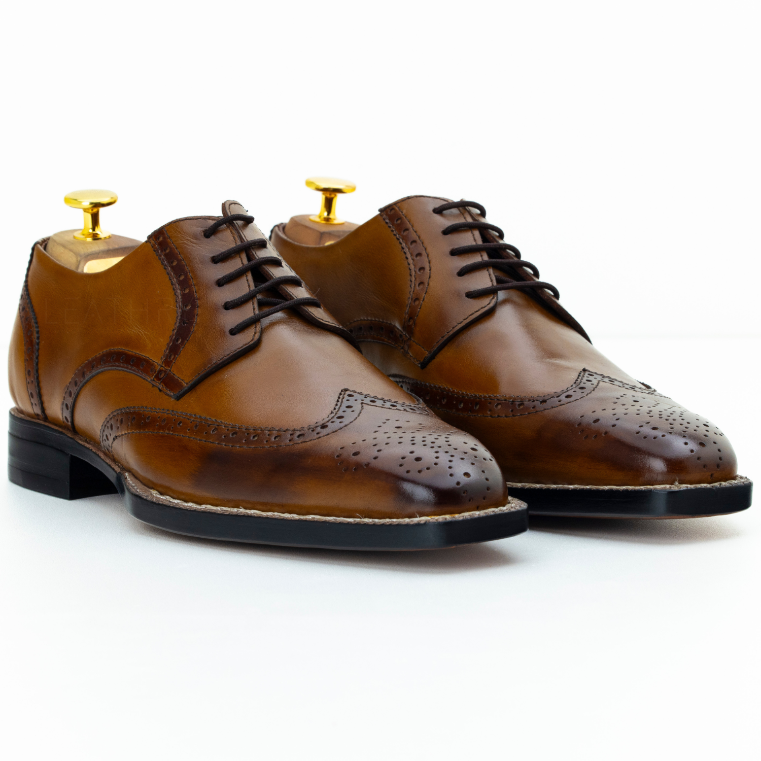 Pair of brown leather dress shoes on gold stands against a white background