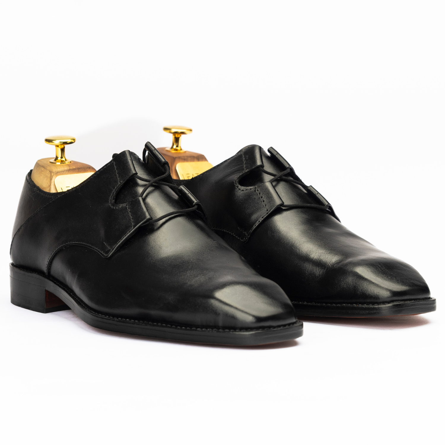 Pair of black dress shoes on gold dress shoe trees against a white background