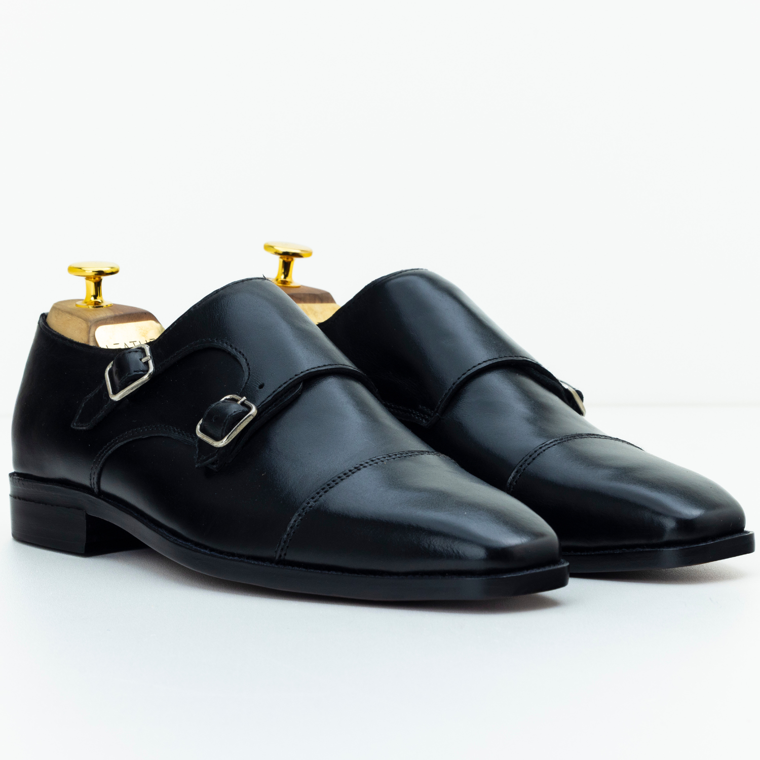 Pair of black leather shoes with gold buckles on a white background