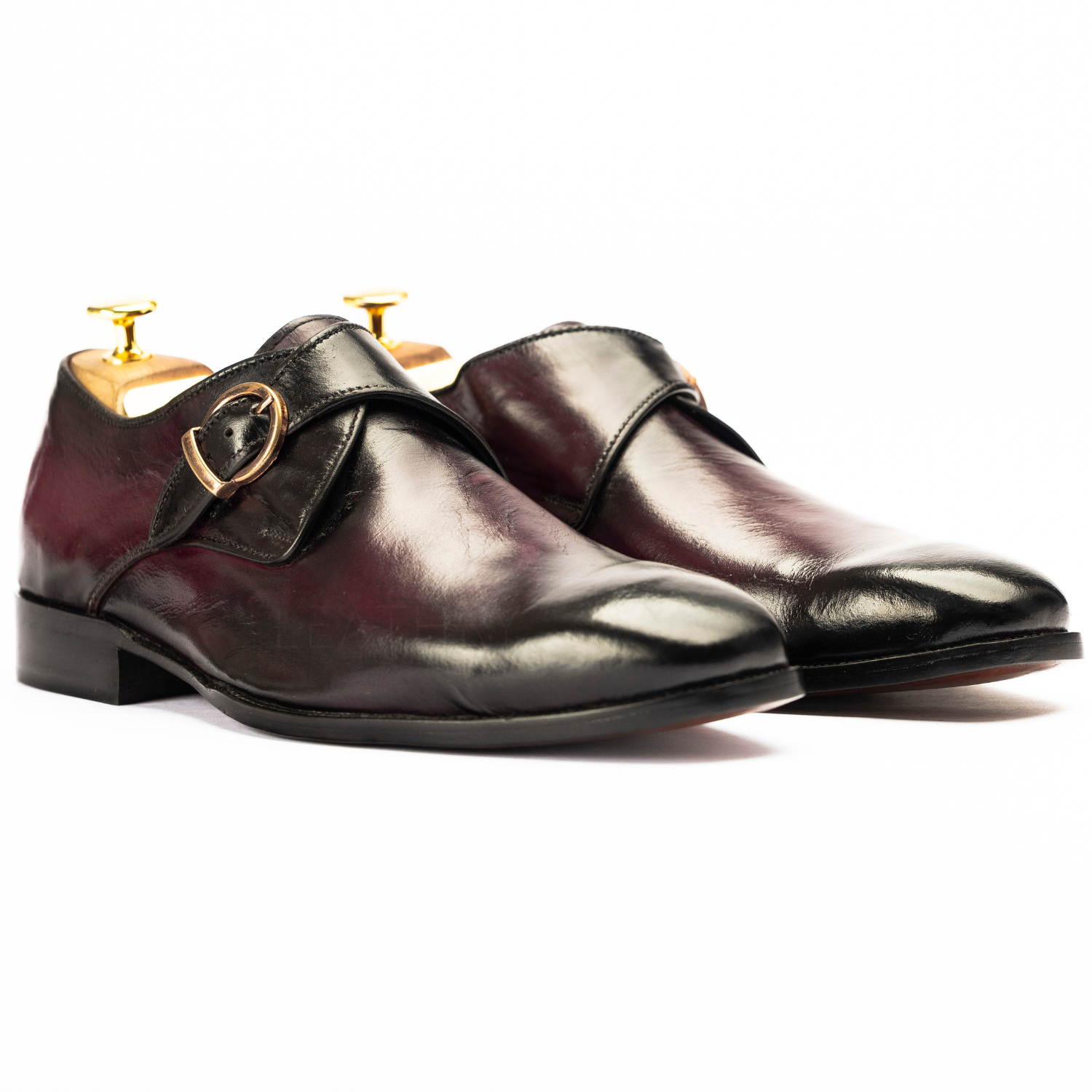 Pair of polished leather shoes with gold buckles on a white background