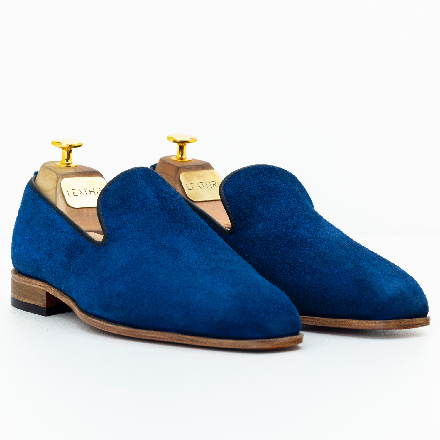 Pair of blue suede loafers on wooden stands with 'Leather' labels against a white background
