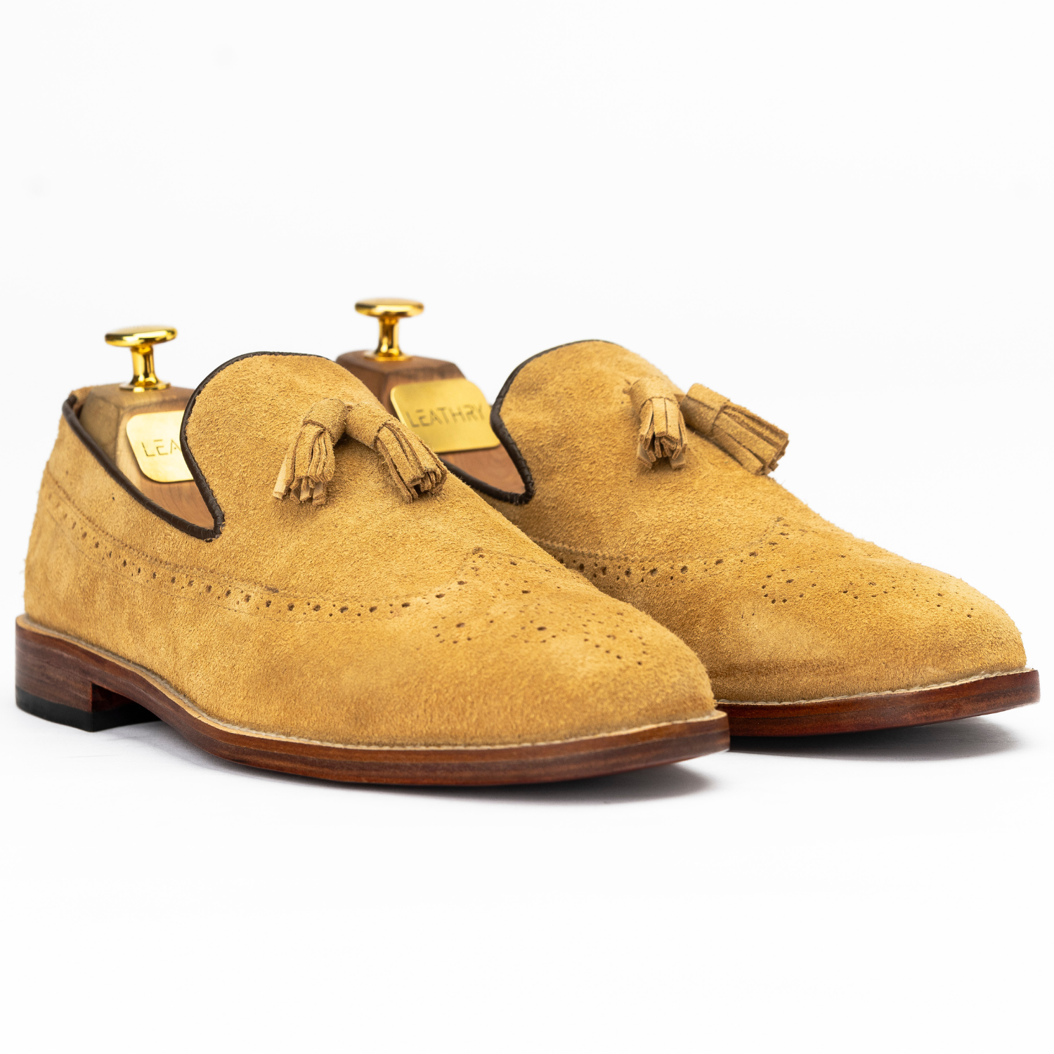 Pair of tan suede shoes with tassels on a white background