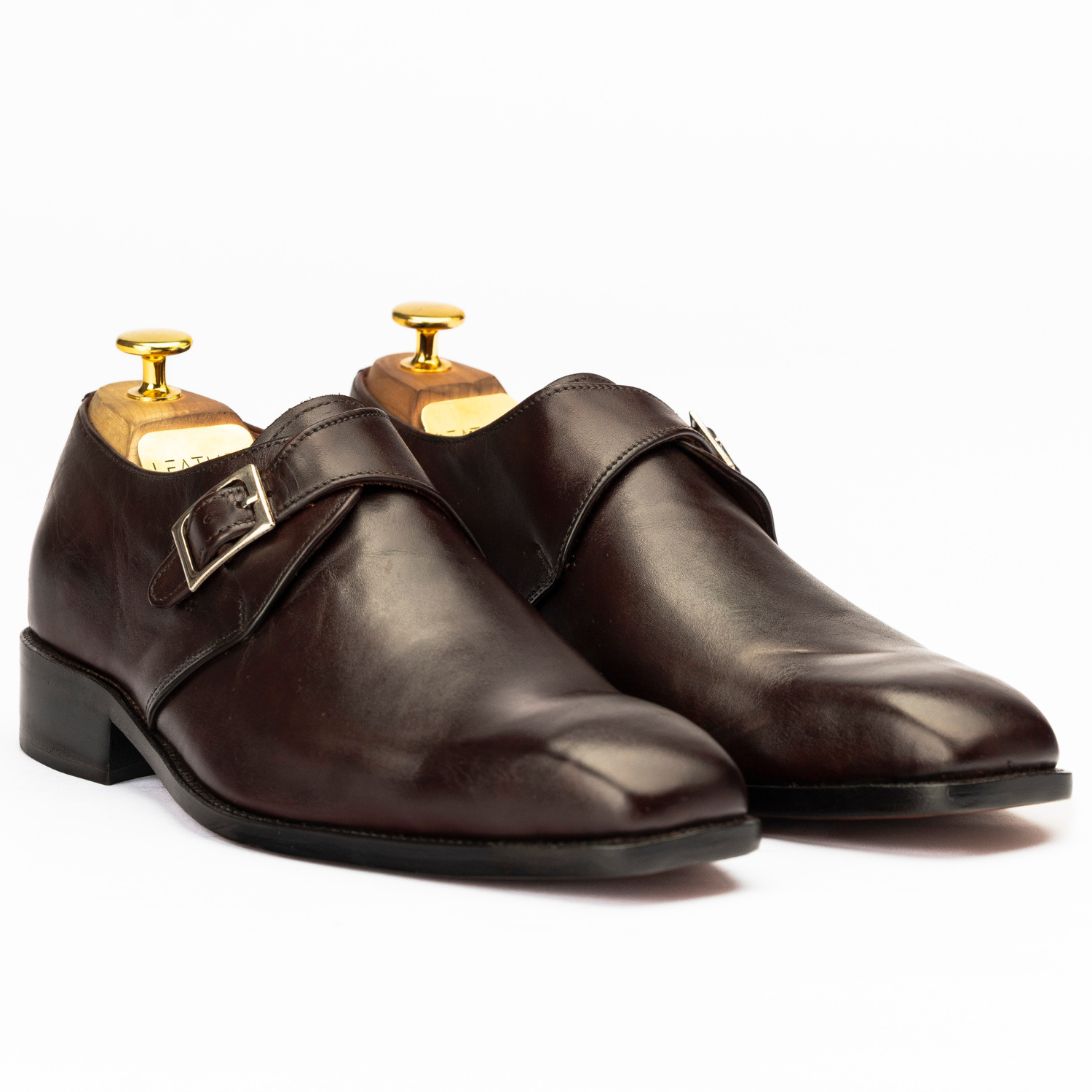 Pair of brown leather shoes with gold buckles on a white background
