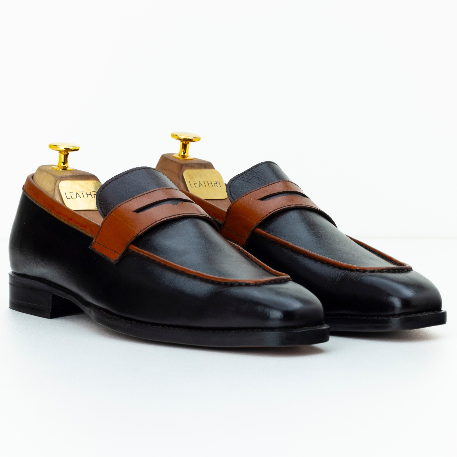 Pair of black leather loafers with brown straps on a white background